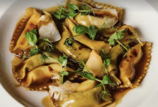 Assiette de raviolis délicatement dressés, nappés de sauce brune et parsemés de jeunes pousses.