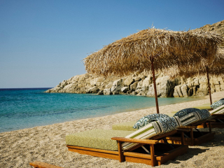 Plage d’Agrari à Mykonos avec chaises longues en bois et parasols en paille