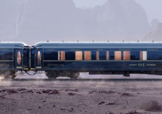 Wagon-lits bleu nuit de l’Orient Express avec inscriptions des destinations historiques, dans un paysage désertique.