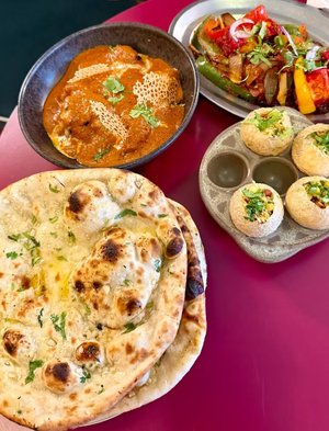 Assortiment de plats indiens colorés sur une table rouge : naan, curry, légumes sautés et amuse-bouches farcis