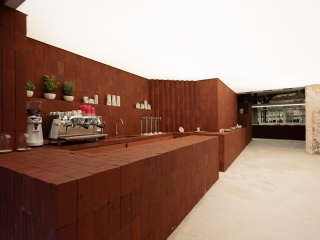Intérieur du coffee shop Saints Pères, avec murs en briques rouges, machine à café, robinets et décorations végétales, comptoir épuré mêlant café et éléments de porcelaine.