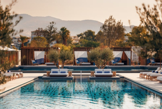 Vue sur la piscine du One&Only Aesthesis sur la Riviera athénienne, entourée d’oliviers et de cabanes contemporaines au coucher du soleil.