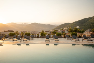 Piscine sur le rooftop du SIRO Boka Place à Tivat, avec vue sur les montagnes de la baie de Boka au coucher du soleil.