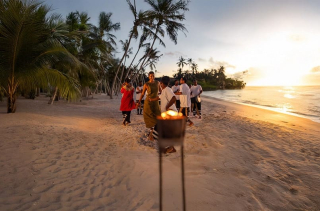 Sur une plage des Maldives, des artistes en tenue traditionnelle dansent au rythme des percussions au coucher du soleil, illustrant l’expérience culturelle “Maldivian Roots”.