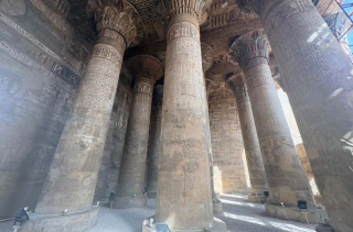 Intérieur du temple d’Esna avec de grandes colonnes ornées de hiéroglyphes et de motifs sculptés.